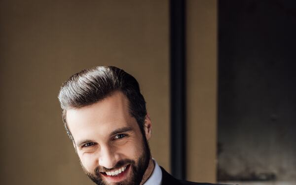 A man in a black suit and red tie, composed.