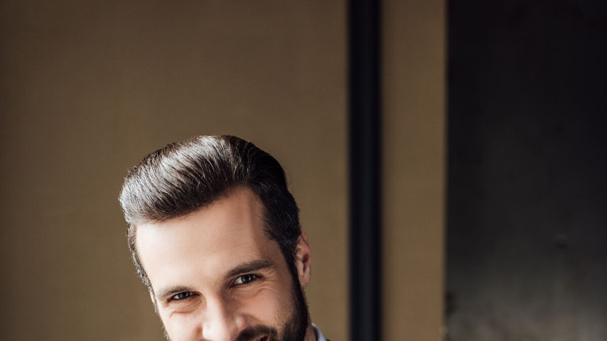 A man in a black suit and red tie, composed, looking off camera.